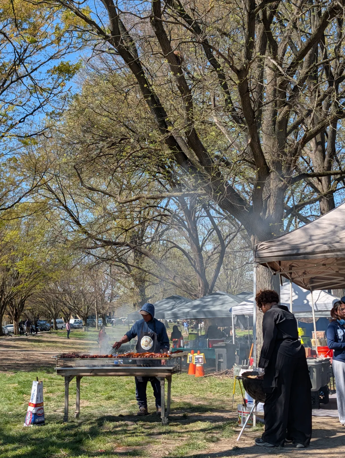 A vendor grilling on a long charcoal grill at the edge of the market