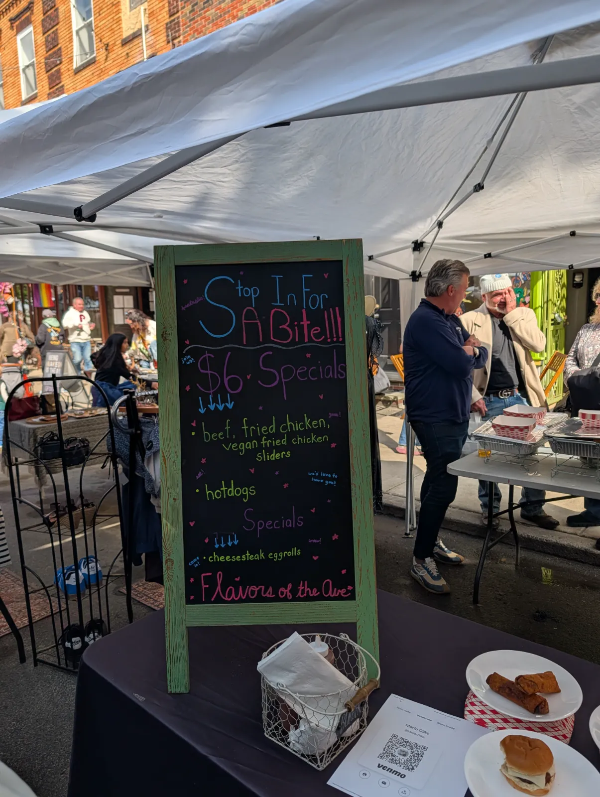 Street food stand offering $6 specials including sliders, hotdogs, and cheesesteak eggrolls