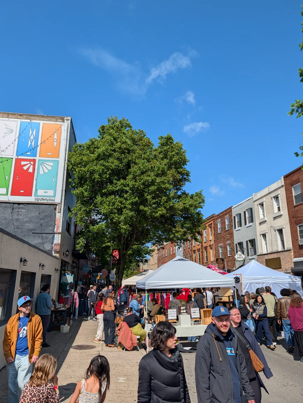 A lively street fair with vendors under white tents and a vibrant community atmosphere under blue sky