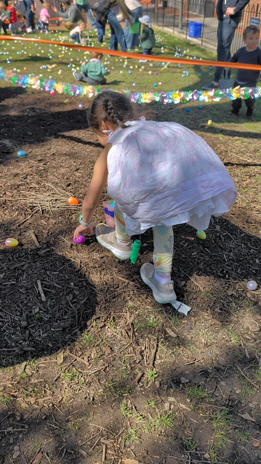 A young child bending down to collect colorful Easter eggs from the ground during an egg hunt