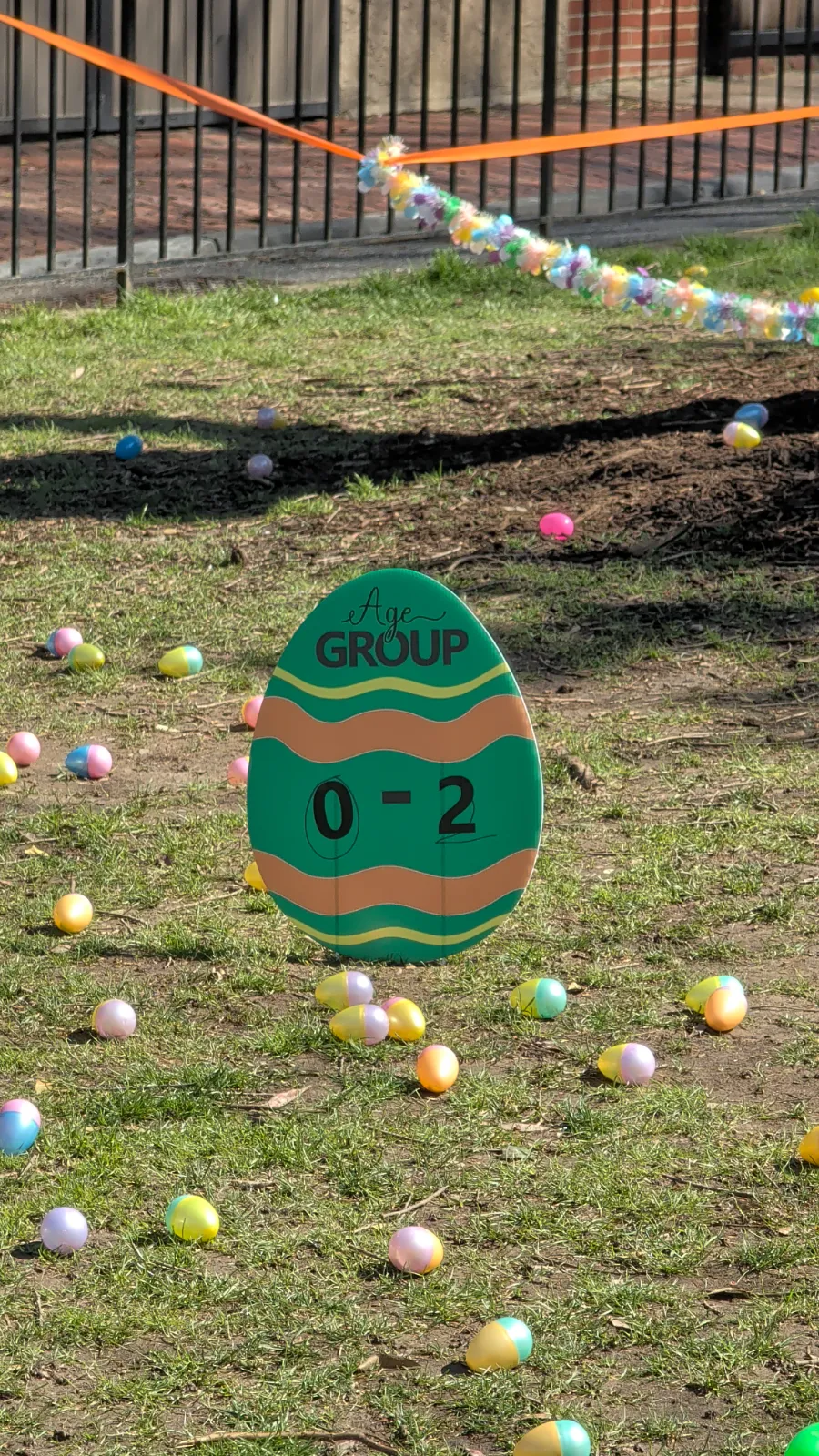Colorful Easter eggs scattered on grass with a sign marking the 0-2 age group area