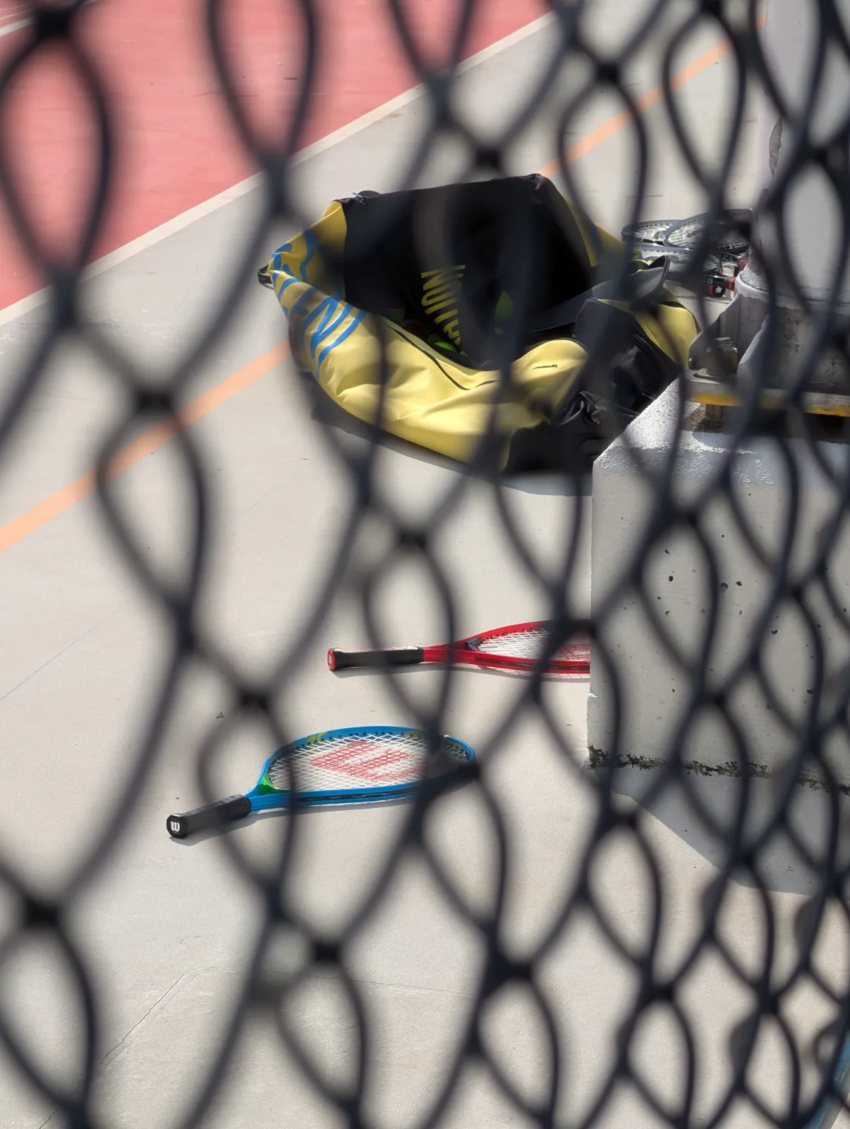 Tennis rackets laying on the court floor, seen through the fence