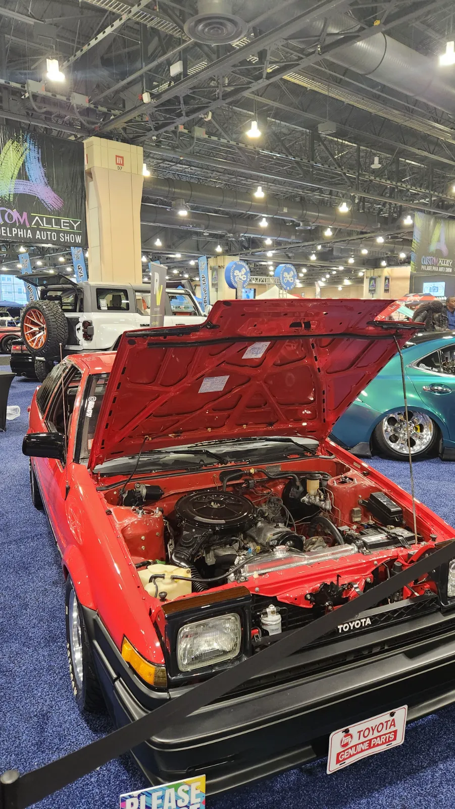 A vibrant red custom Toyota with a detailed engine bay on display at the Philadelphia Auto Show