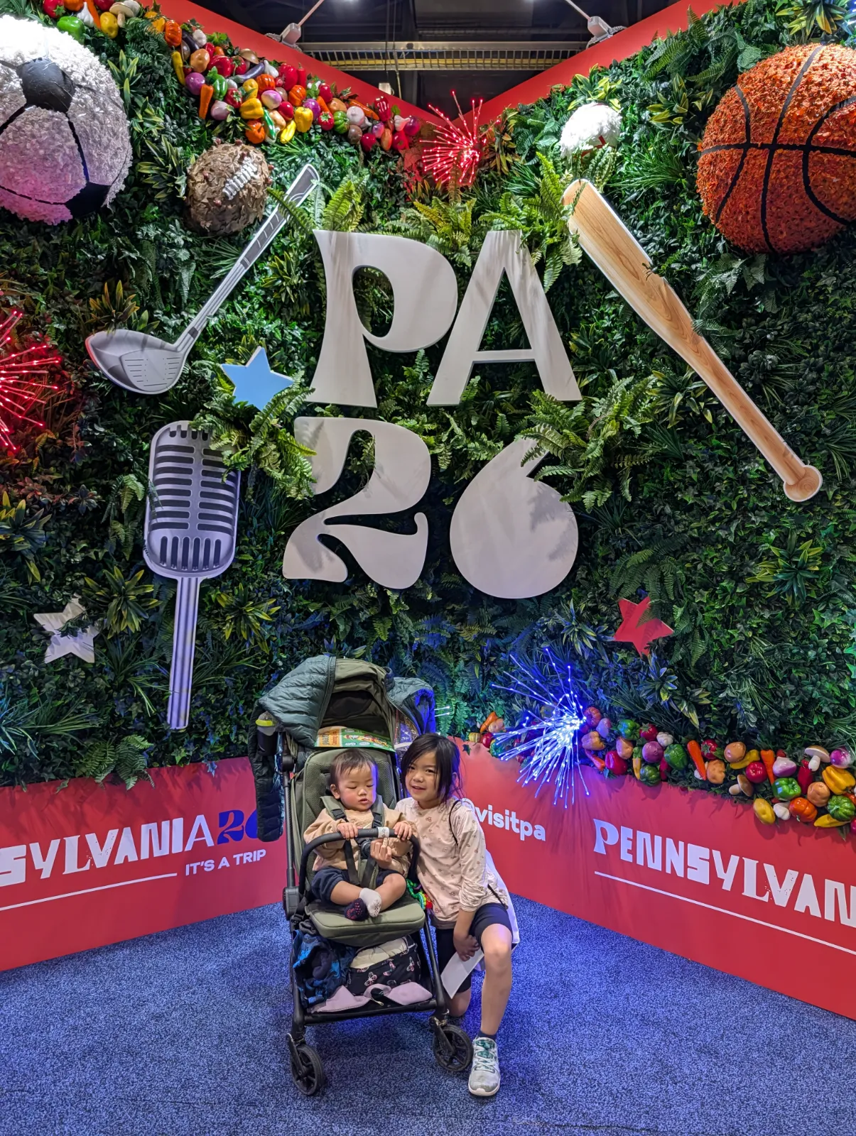 Two kids posing in front of a colorful Pennsylvania attractions wall at the Auto Show