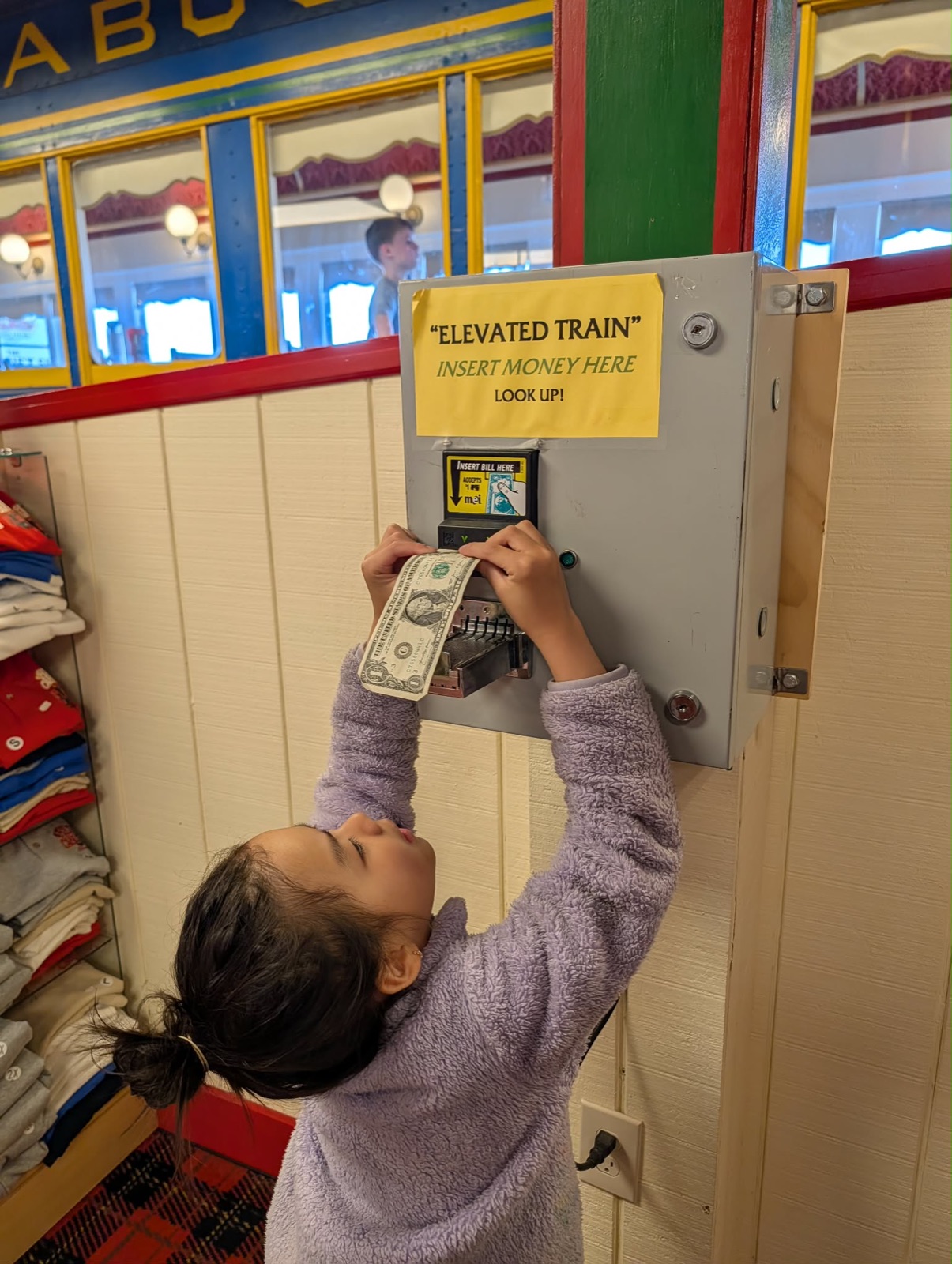 Charlotte putting a dollar into the elevated train machine at the Red Caboose gift shop