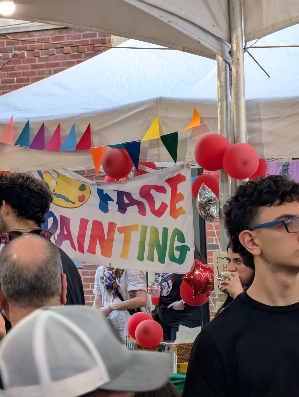 Colorful face painting sign with festive bunting and red balloons at the Lebanese Festival
