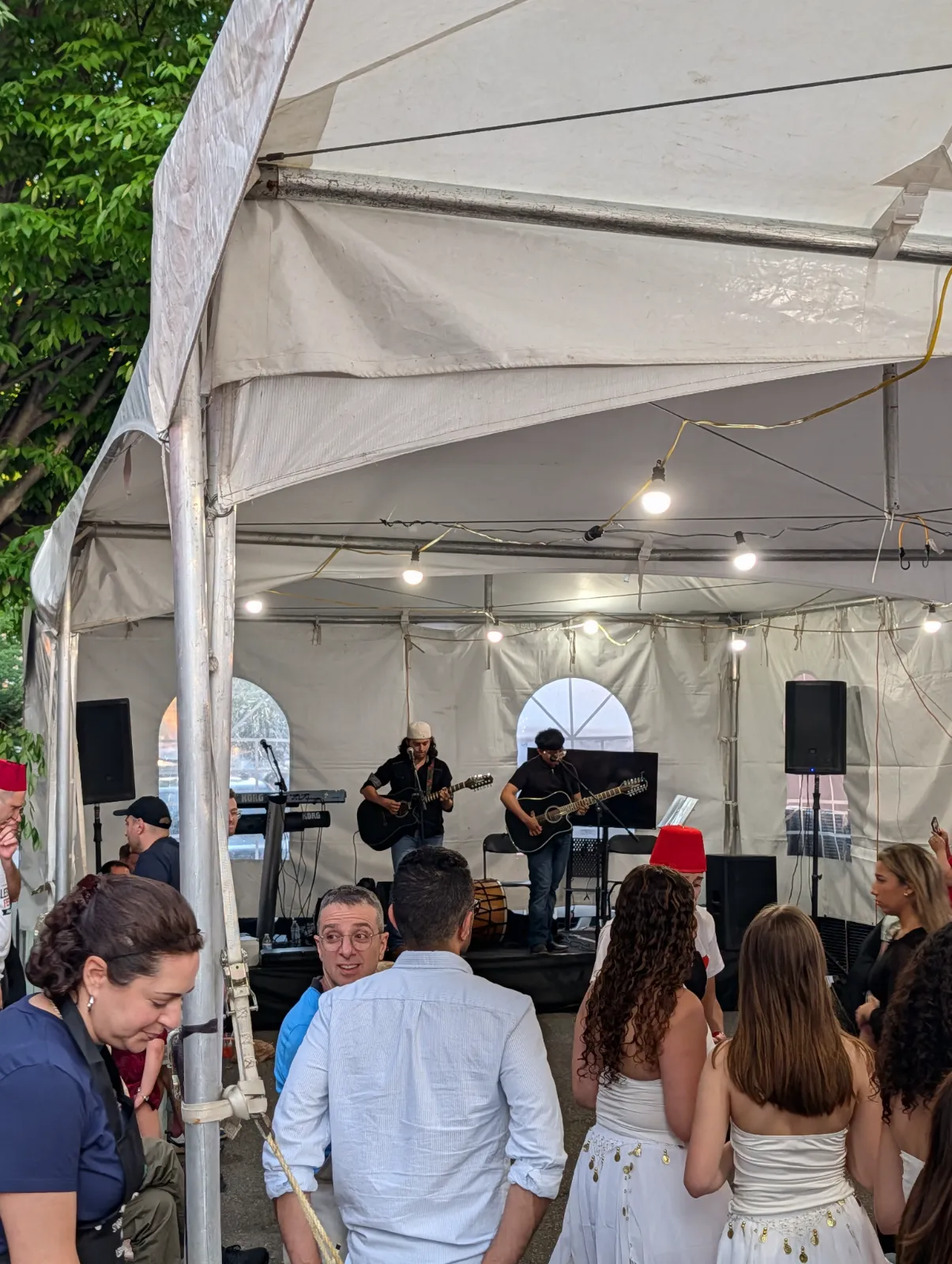 Musicians performing under a large tent at the Lebanese Festival surrounded by engaged attendees in festive attire