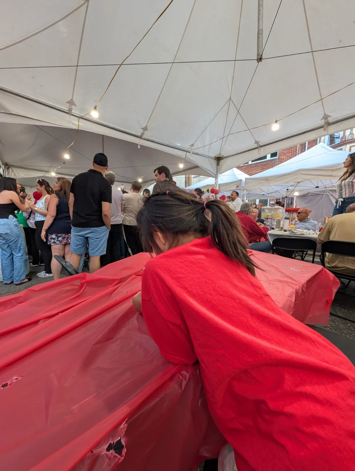 Families enjoying the Lebanese Festival under a large tent with a child in a red shirt leaning over a table