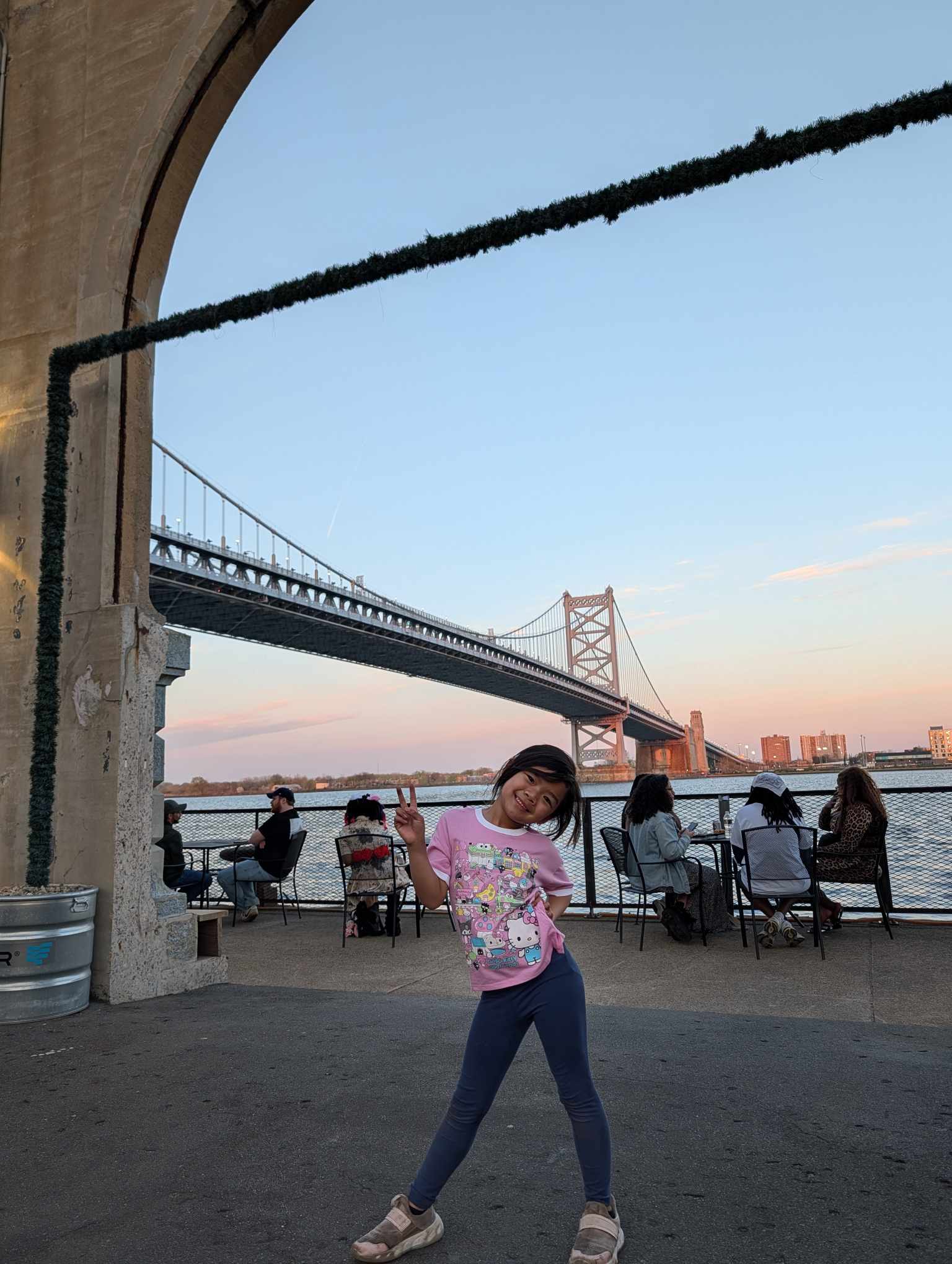 Charlotte posing at the pier with the Ben Franklin Bridge and sunset behind her