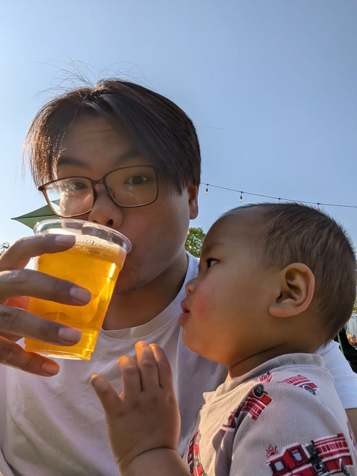Brandon holding Parker at Parks on Tap while the toddler curiously reaches for a drink