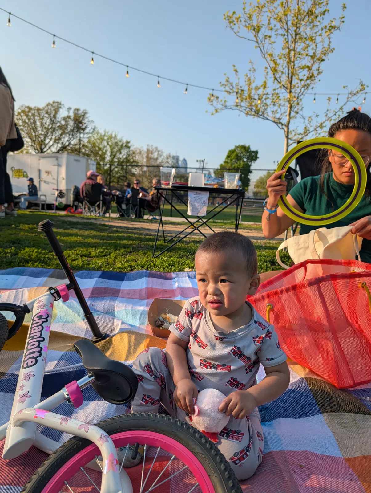 A toddler sitting on a colorful blanket next to a small bike at the park