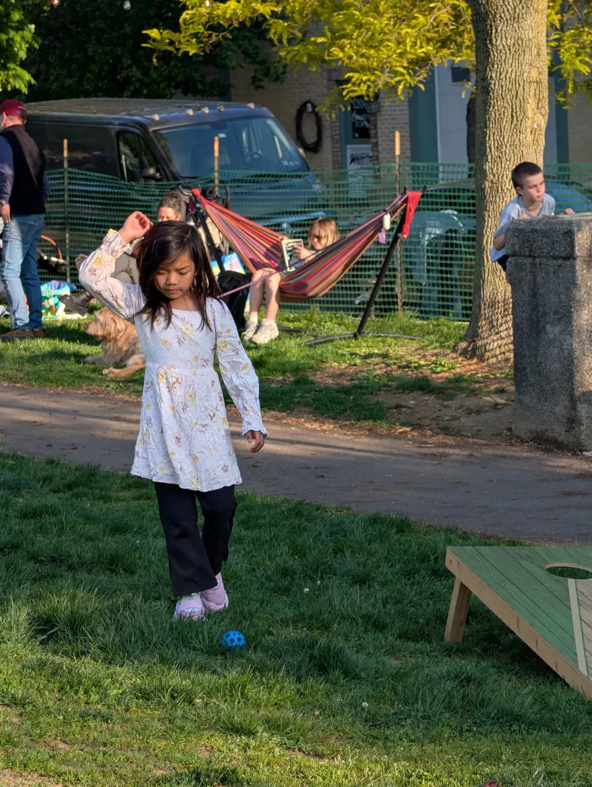 A girl playing with a ball at the park while families enjoy activities in the background