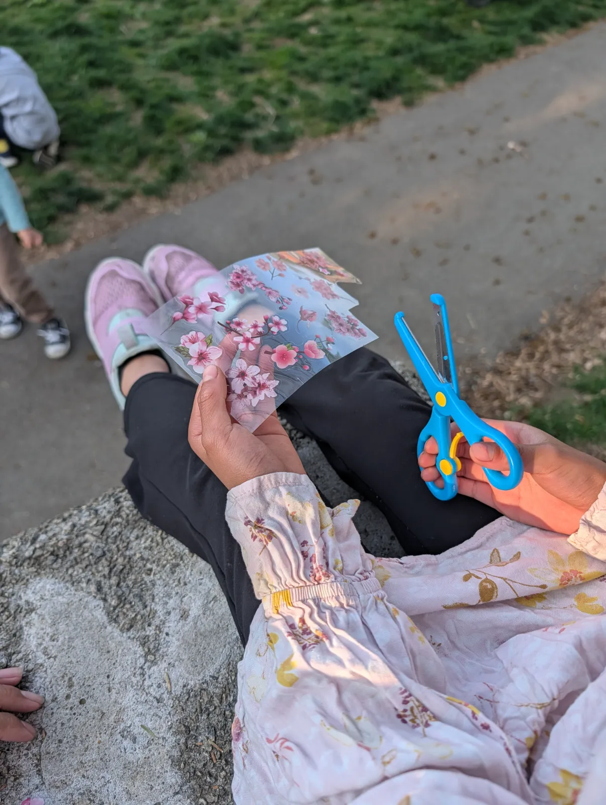 A child's hands holding floral stickers and scissors during a crafting session at the park
