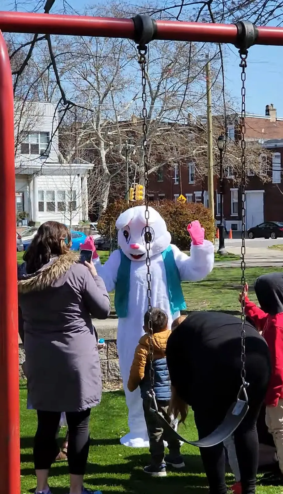 A cheerful Easter bunny mascot entertaining children at a park while families capture the moment