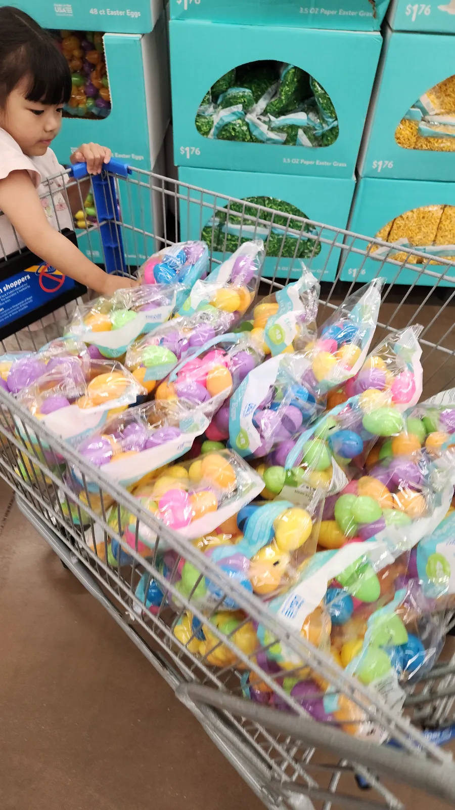 A child pushing a shopping cart filled with colorful Easter eggs during hunt prep